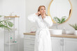 © Pixel-Shot - Beautiful happy mature woman in bathrobe doing face building exercise at home