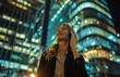 © yevgeniya131988 - Smiling businesswoman talks on phone by skyscraper at night in suit, blouse, and shirt