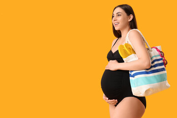 Poster - Young pregnant woman in swimsuit holding bag on yellow background. Travel concept