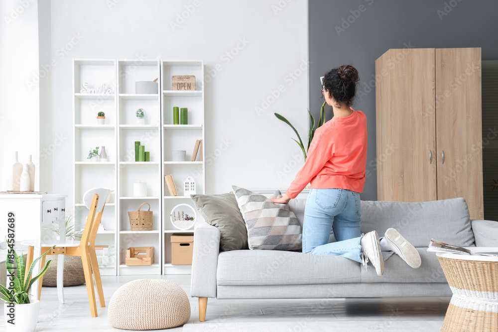 Young woman turning on air conditioner at home, back view