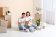 © Pixel-Shot - Young happy couple sitting and unpacking belongings in their new house