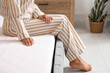 © Pixel-Shot - Young woman sitting on soft mattress in bedroom, closeup