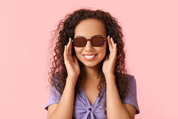 Wall Mural - Happy young African-American woman in sunglasses on pink background