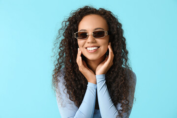 Wall Mural - Happy young African-American woman in sunglasses on blue background