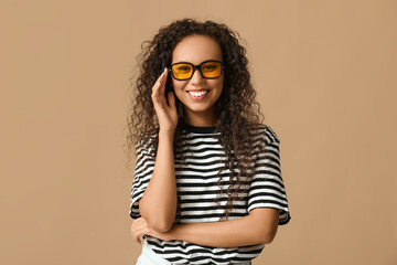 Wall Mural - Happy young African-American woman in sunglasses on beige background