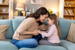 © Graphicroyalty - A young family shares a tender moment. A child daughter holding their mother's arms, both smiling with love and joy. They relax on the living room sofa, cherishing quality time together.