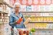 © StockPhotoPro - Senior customer comparing products at the supermarket