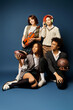 © LIGHTFIELD STUDIOS - A group of young multicultural friends, sitting next to each other in stylish attire on a dark blue background.