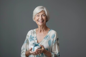 Wall Mural - Portrait of a grinning caucasian woman in her 60s holding a gift isolated on soft gray background