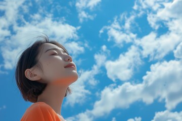 Young asian woman looking up with closed eyes, blue sky with clouds on the background, happy life