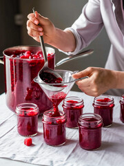 Poster - a person is ladling raspberry jam into glass jars using a stainless steel ladle. 