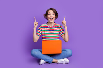 Wall Mural - Photo of cheerful excited girl dressed trendy clothes sitting floor presenting novelty empty space isolated on violet color background