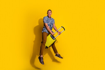 Sticker - Full length photo of attractive funny guy wear print shirt riding suitcase jumping emtpy space isolated yellow color background