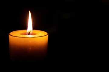 close-up single flame of a burning candle on a black or dark background with copy space. Concept of mourning, memory and sorrow.