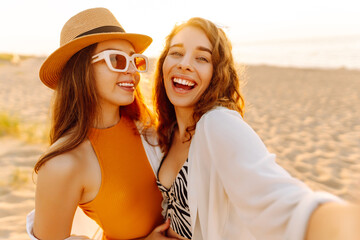 Wall Mural - Cheerful women making selfie while having fun on the beach. Friends together. Travel, blogging, weekend, relax and lifestyle concept.