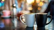 © IYearDesign - Coffee and a Good Conversation, Two coffee mugs placed next to each other on a table with a blurred background of two people talking Casual attire like a blazer or a blouse