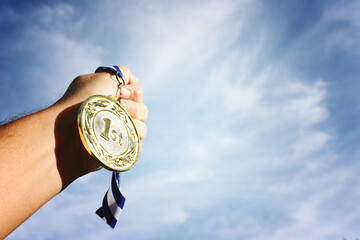 Wall Mural - man hand raised, holding gold medal against sky. award and victory concept