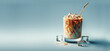 © Elena - Old-fashioned tumbler of iced coffee swirls coffee and cream for marbling effect. Gold metal straw, surrounded by ice cubes, against soft blue gradient background,