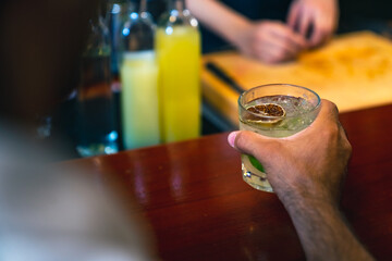 Poster - Professional male bartender preparing and serving cocktail drink to customer on bar counter at luxury nightclub. Barman making mixed alcoholic drink for celebrating holiday party at restaurant bar.