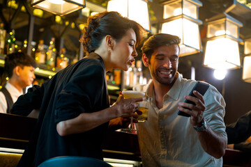 Wall Mural - Caucasian man and woman using mobile phone for online booking or making payment during hanging out nightlife party at restaurant bar. People enjoy meeting nightlife celebration party at nightclub.