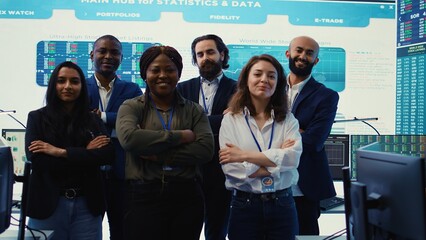 Diverse group of business professionals posing together in monitoring room, multinational company headquarters. Executive management team working with big data screen in the office. Camera B.