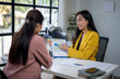 © Wasana - Two women are sitting at a desk with a yellow jacket on one of them