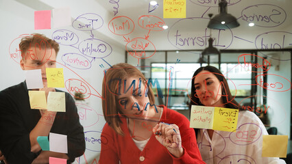 Wall Mural - Creative business team brainstorming and sharing marketing idea about start up project by writing down on colorful sticky note at glass board modern meeting room. Working together. Immaculate.