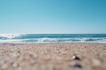 Wall Mural - Tranquil and endless ocean view, captured from a sandy perspective, with sun glinting off gentle waves under a clear blue sky