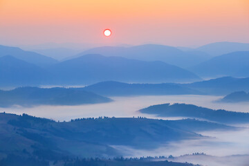 Wall Mural - mountain chain silhouette in dense mist at the sunrise