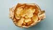 © NK - Crispy potato chips in a crinkled paper bag on a light blue background, close-up shot. Snack and junk food concept