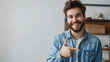 © john - Caucasian young male in denim shirt grins at camera, indicates at copy space, advertises something. Happy bearded man points with fore finger, has satisfied expression, smiles. Look here!