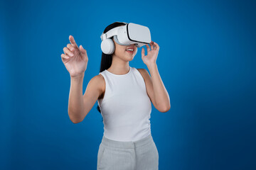 Smart female standing with blue background wearing VR headset connecting metaverse, futuristic cyberspace community technology. Elegant woman excited seeing generated virtual scenery. Hallucination.