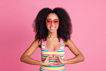 Sticker - Portrait of lovely thankful girl with curly hairstyle wear colorful top in glasses showing heart symbol isolated on pink color background