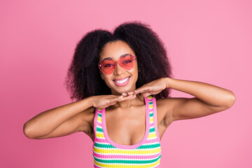 Portrait of cute girl with curly hairstyle wear colorful top in glasses holding hands under chin isolated on pink color background