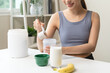 © Pormezz - Young sporty woman pouring protein powder into a cup to make replacement food meal after workout