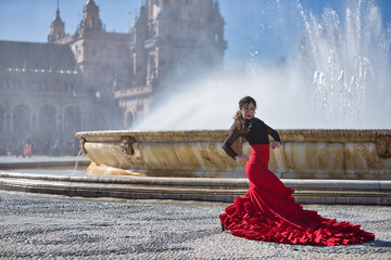 Wall Mural - Young, beautiful, brunette woman in black shirt and red skirt, dancing flamenco in front of a beautiful fountain in Spain square in Seville. Flamenco concept, dance, art, typical Spanish.