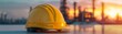 © ธนากร บัวพรหม - Industrial scene with a yellow safety helmet on a table, refinery structures in the background at golden hour, highlighting construction safety, clear and warm