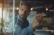© Formoney - A man with a beard is looking at a graph on a window