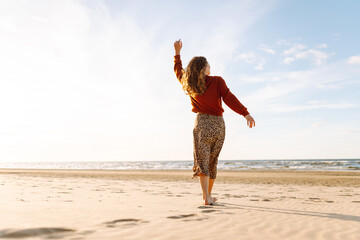 Wall Mural - Carefree woman  relaxing on coast at sunset. Windy autumn days. The concept of relaxation, enjoyment, solitude