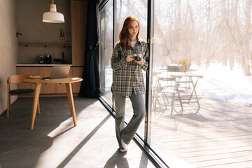 full length portrait of pretty woman drinking enjoying hot coffee, smiling looking away, standing by
