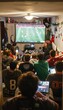 © spyrakot - College Students Enthusiastically Watching Soccer Game in Packed Dorm Room - Fun and Excitement