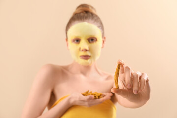 Wall Mural - Young woman with turmeric sheet mask and roots on beige background, closeup