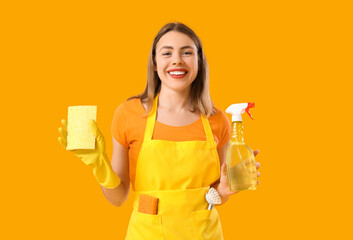 Wall Mural - Young woman with bottle of detergent and cleaning sponge on orange background