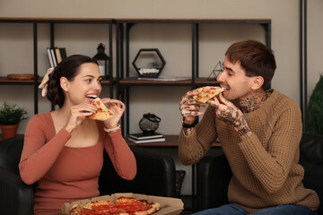 Canvas Print - Happy young couple eating tasty pizza and sitting on armchairs at home