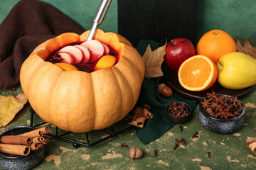 Wall Mural - Beautiful composition with tasty mulled wine in pumpkin on green background