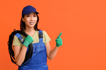 Wall Mural - young female electrician with cables pointing at something on orange background