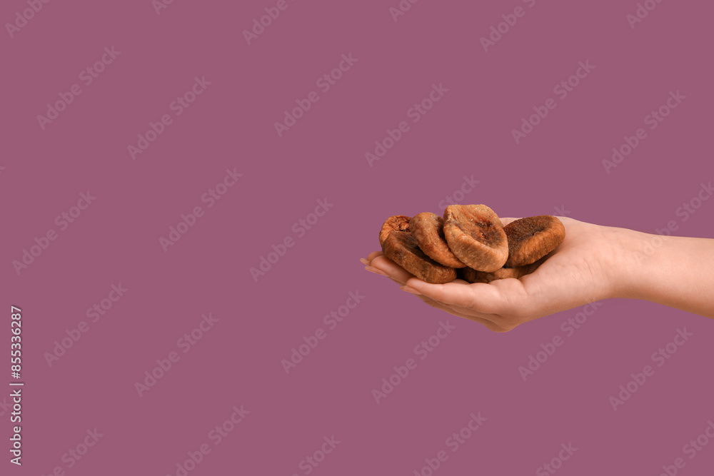Female hand with tasty dried figs on purple background