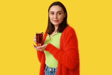 Wall Mural - Beautiful young woman with glass cup of hot mulled wine on yellow background