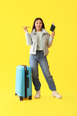 Wall Mural - Young woman with wooden plane, passport and suitcase on yellow background