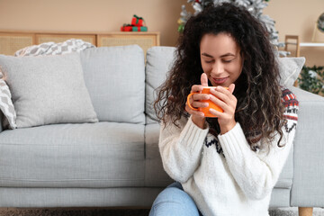 Sticker - Beautiful young African-American woman with cup of hot mulled wine at home